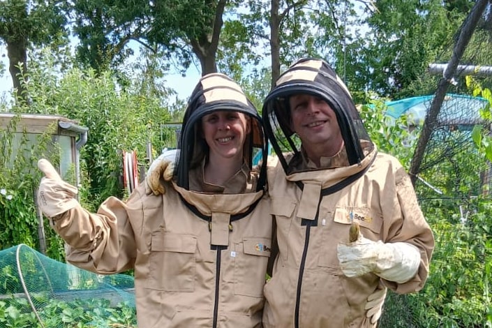 Twee imkers in beschermende kleding bij de bijenstand.